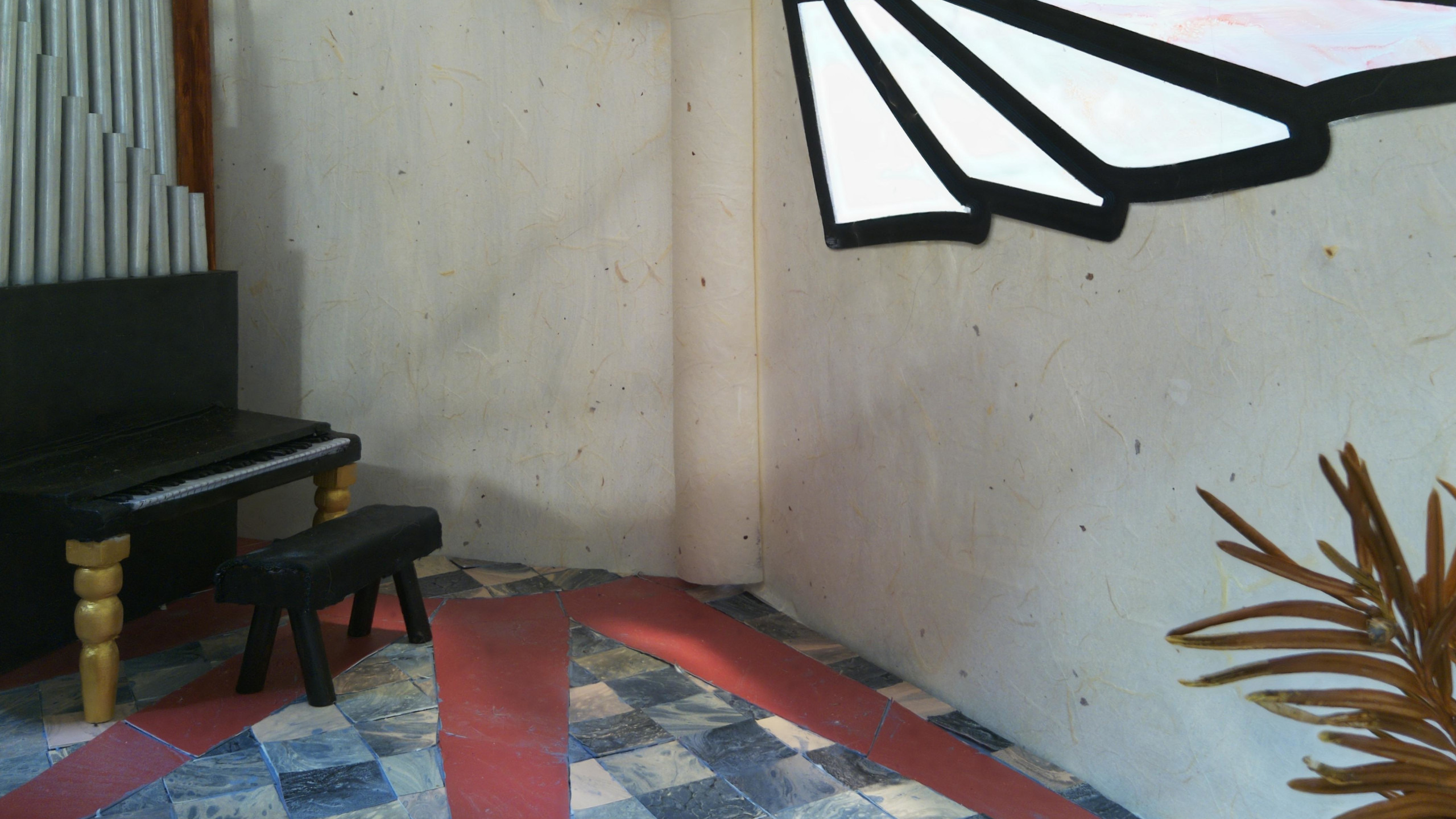 In a corner of a room sits a pipe organ.  There's a wing-shaped window on the left.  The floor is marble tile with a red sunburst pattern against grey-and-cream squares.