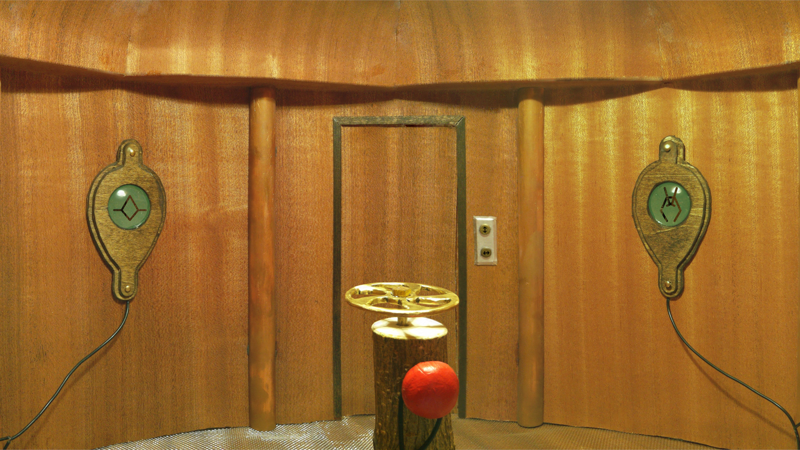 The inside of a round room with woodend walls and a wooden ceiling.  We're facing a wood door.  Next to the door are two buttons labeled with opposing arrows.  To the left and right are oblong walnut frames holding lenses looking onto weird symbols.  In the foreground, a plinth holds a brass crankwheel and a big red button.